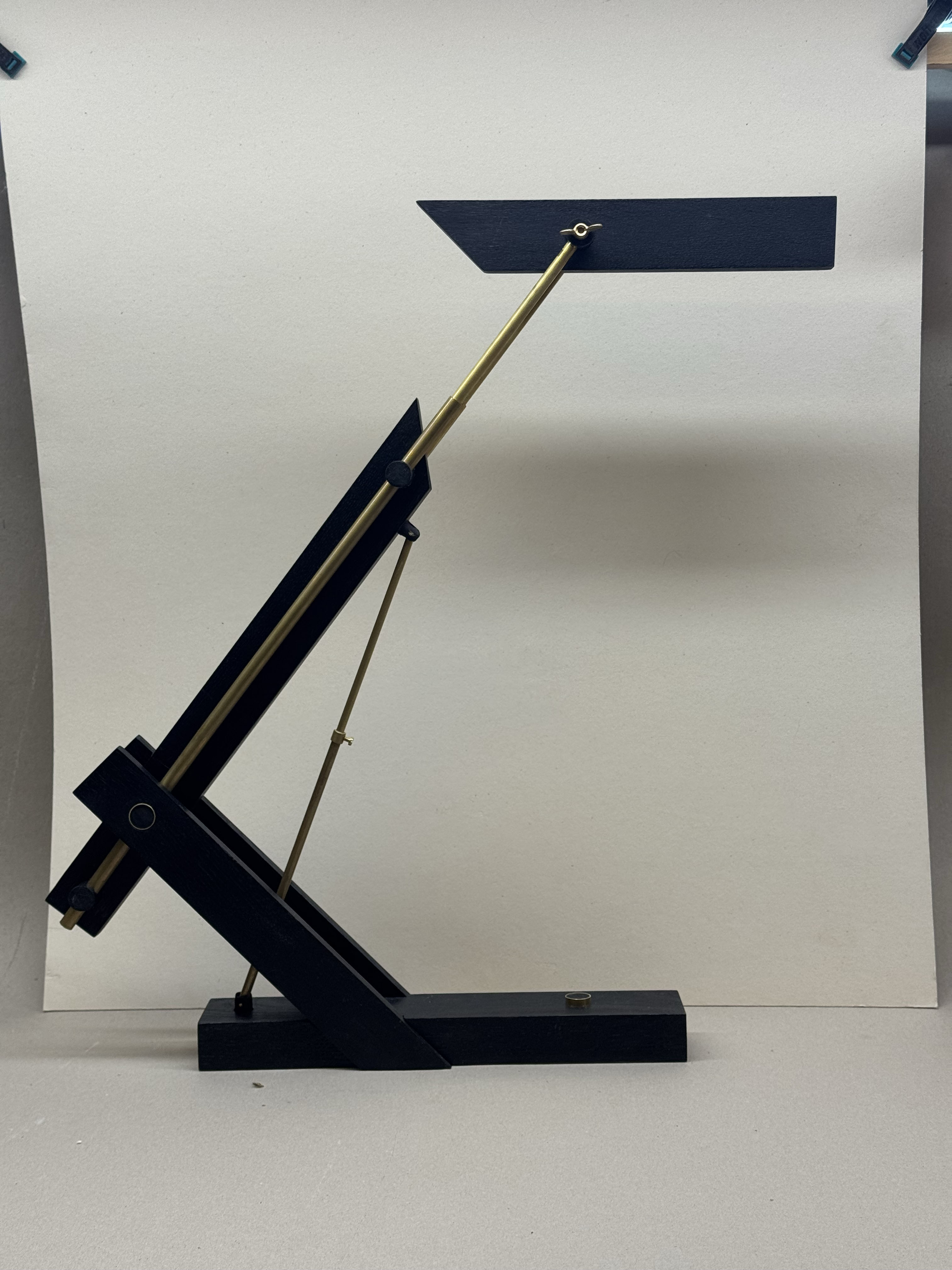 Minimalist modern black desk lamp with brass adjustable arm and rectangular shade against a plain light background.