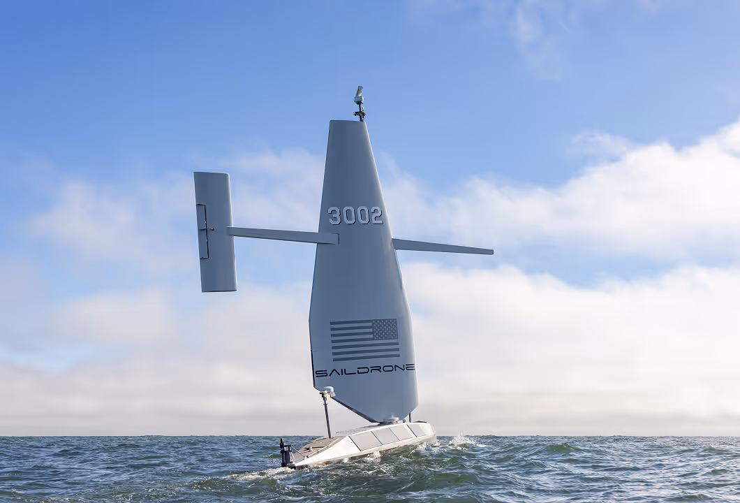 Saildrone unmanned vehicle on ocean water under blue sky with clouds.
