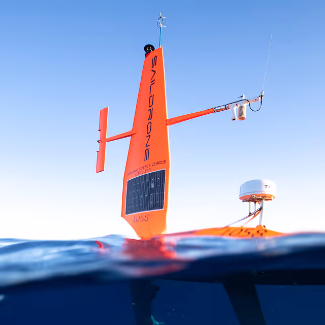 Orange Saildrone advanced science vehicle floating on the water surface against a clear blue sky.