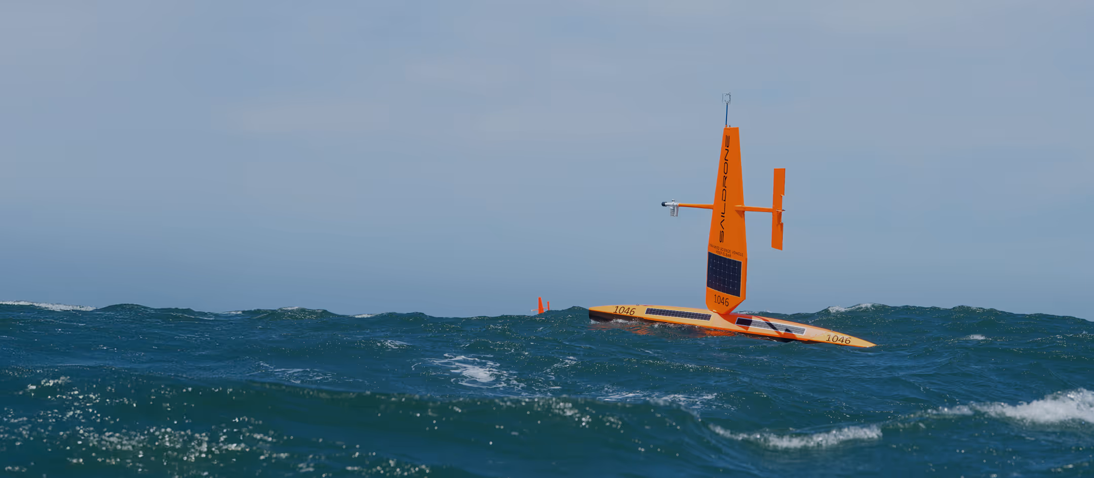 Orange Saildrone autonomous sailing vehicle floating on choppy ocean water under clear sky.
