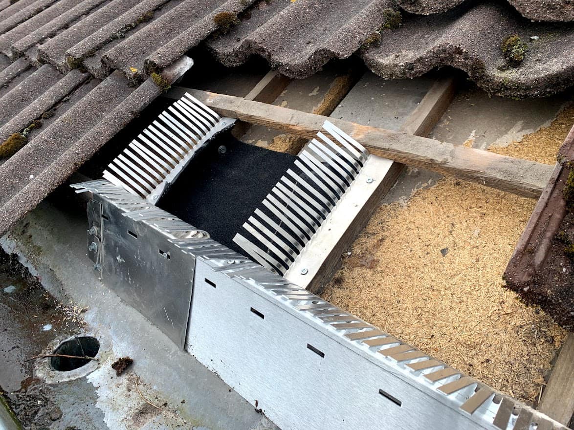 Reparatie van een gat in het dakbeschot onder dakpannen, vermoedelijk veroorzaakt door een steenmarter, met zichtbare houten balken en een metalen rooster ter preventie.