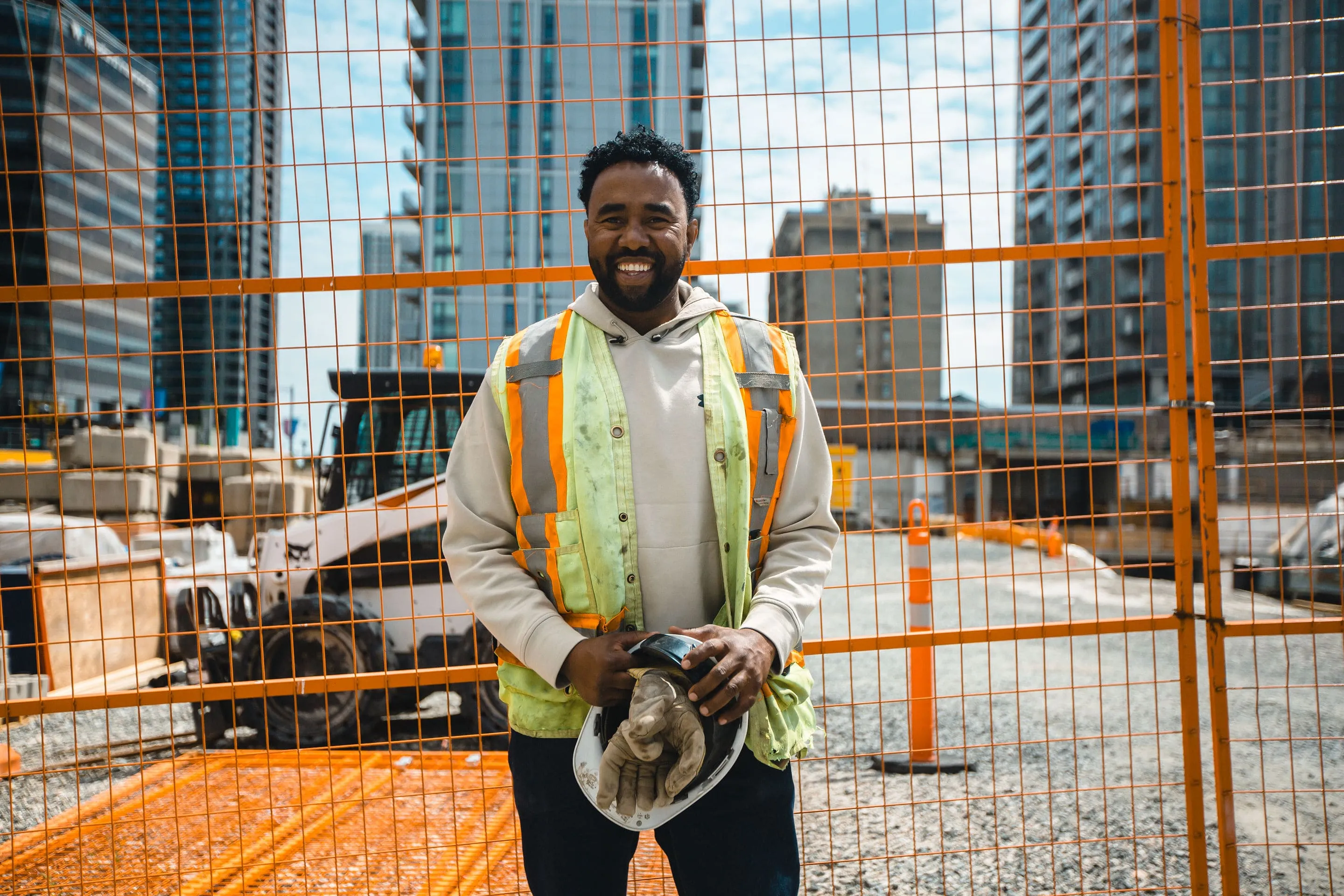 Kebrid wearing a reflective vest, standing in front of a construction field