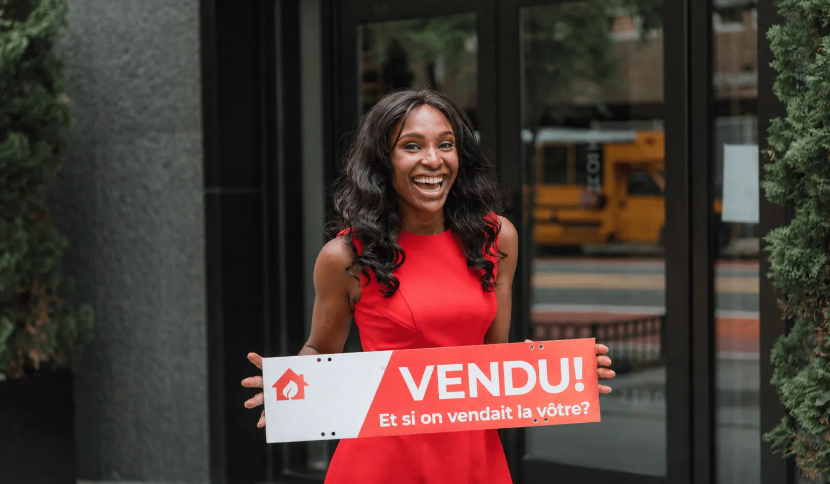 Une femme souriante tenant une pancarte « VENDU ! »