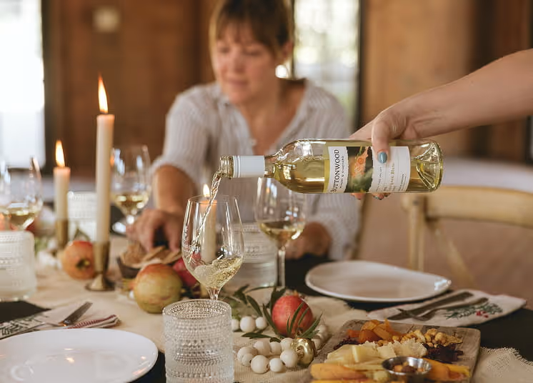 Buttonwood Sauvignon Blanc being poured into a glass at an elegant dinner table set with candles and charcuterie