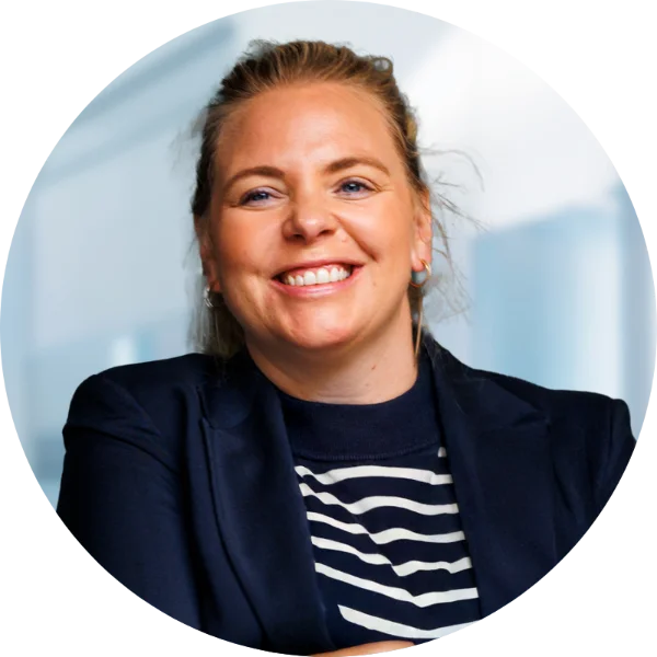 Leende kvinna med blont hår uppsatt, klädd i marinblå kavaj och randig skjorta.