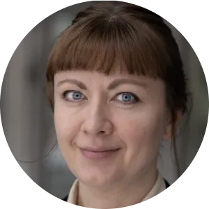 Smiling woman with blonde hair tied back, wearing a navy blazer and striped shirt.