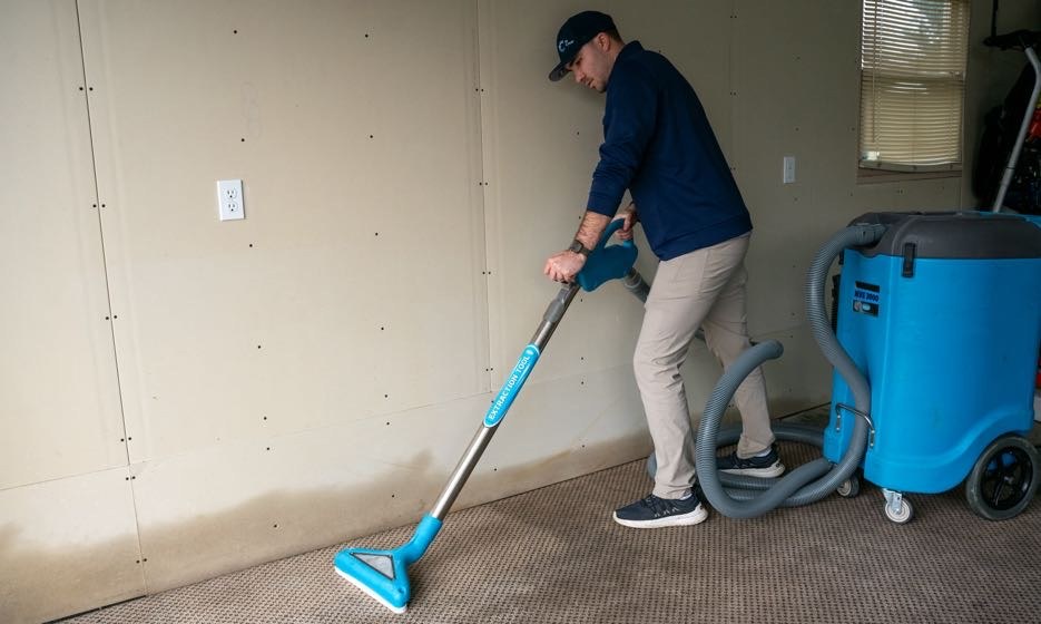 Technician extracting water from wet carpet with a commercial extractor and wand
