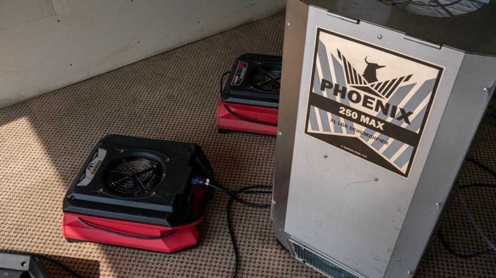 Commercial dehumidifier and low-profile air movers set up to dry a water-damaged room