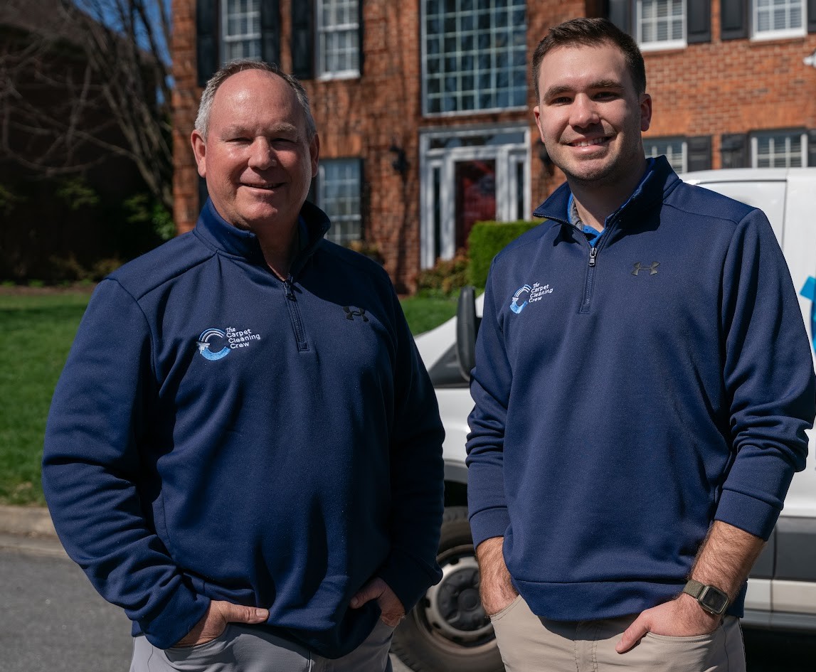 David Wilson (left) and his son Seth Wilson, owners of The Restoration Crew, smiling outside in navy company pullovers