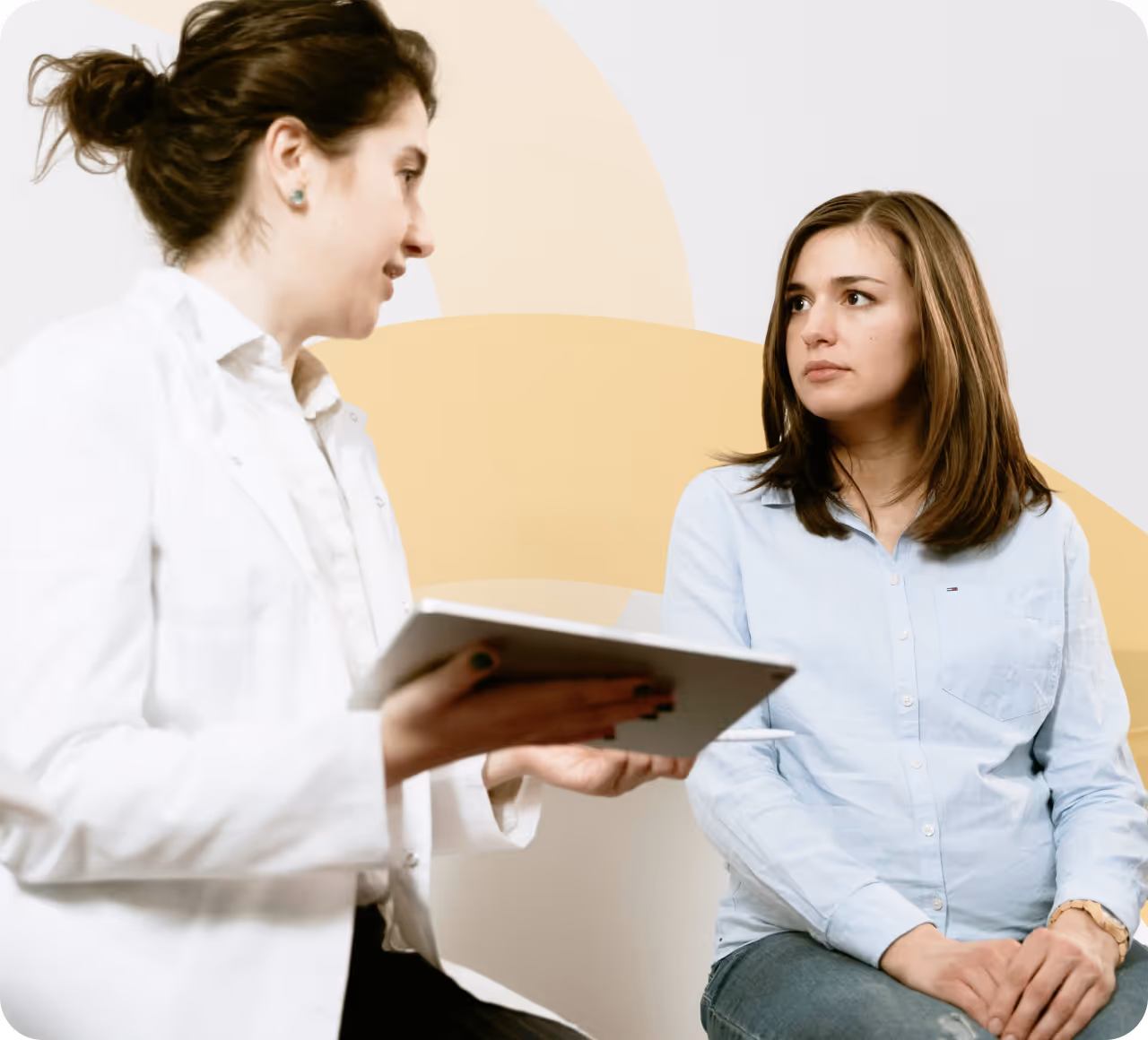 A woman talking to another woman in front of a wall.