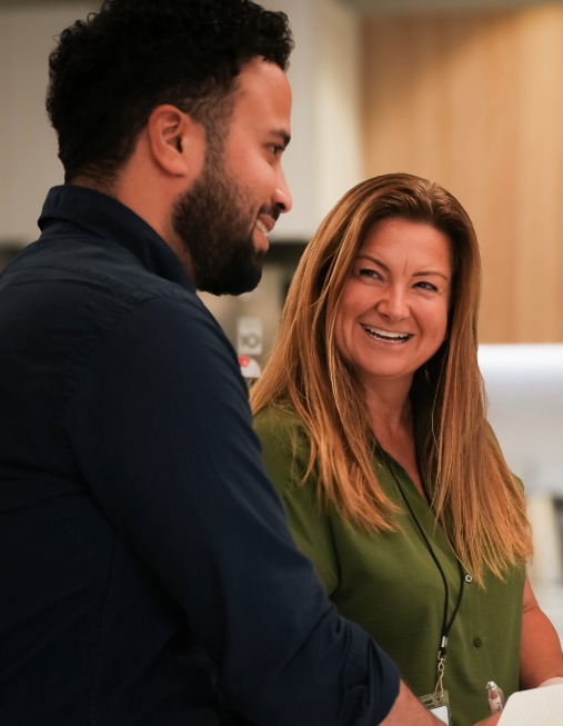 A man smiles while talking to a woman in a bright office.