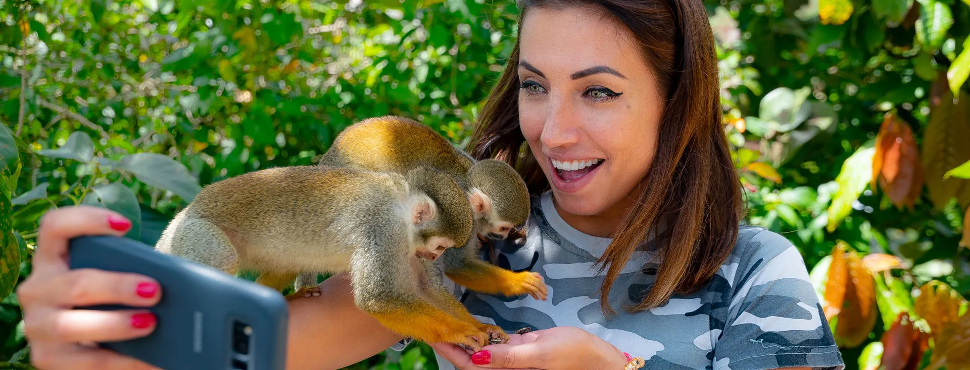 Traveller taking a selfie with squirrel monkeys perched on her arm in a tropical forest