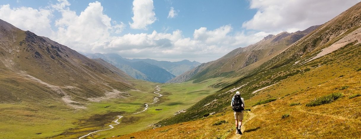 Hiker with a backpack walking a narrow trail high above a green mountain valley