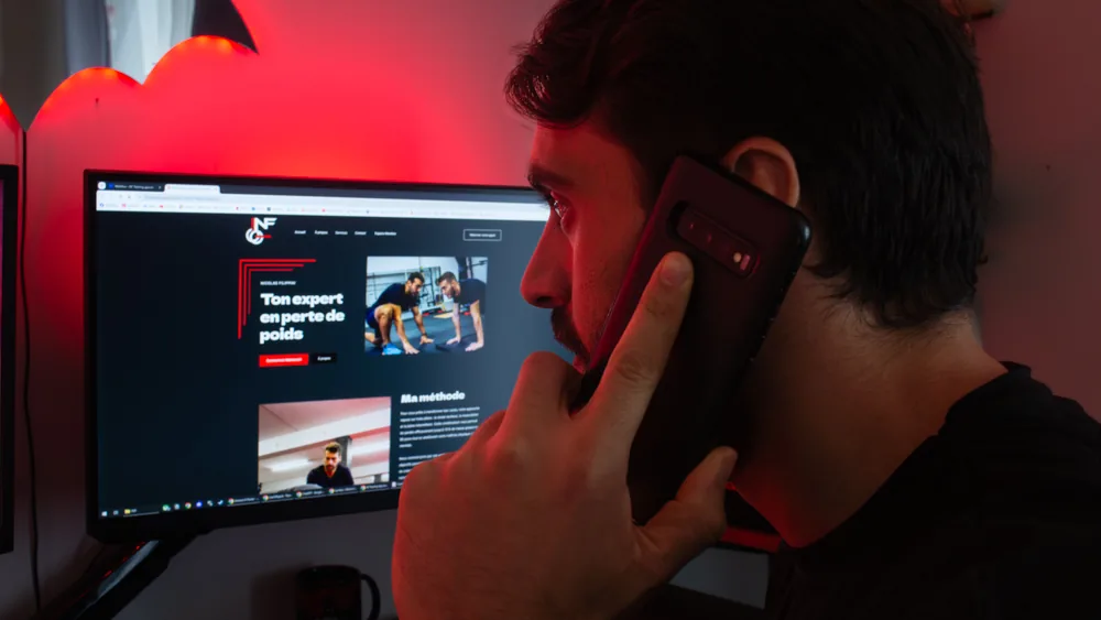 Un homme de profil, téléphone à l'oreille, devant un écran qui affiche le site NF Training.