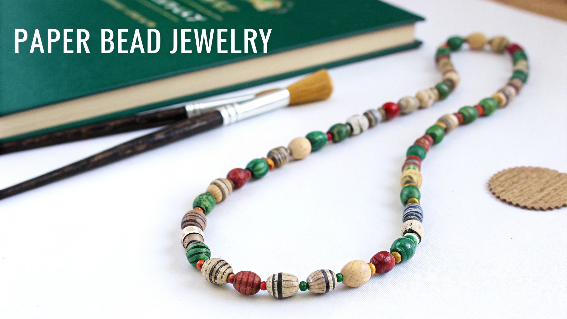 Colorful handmade paper bead necklace with green, red, and tan beads next to craft supplies