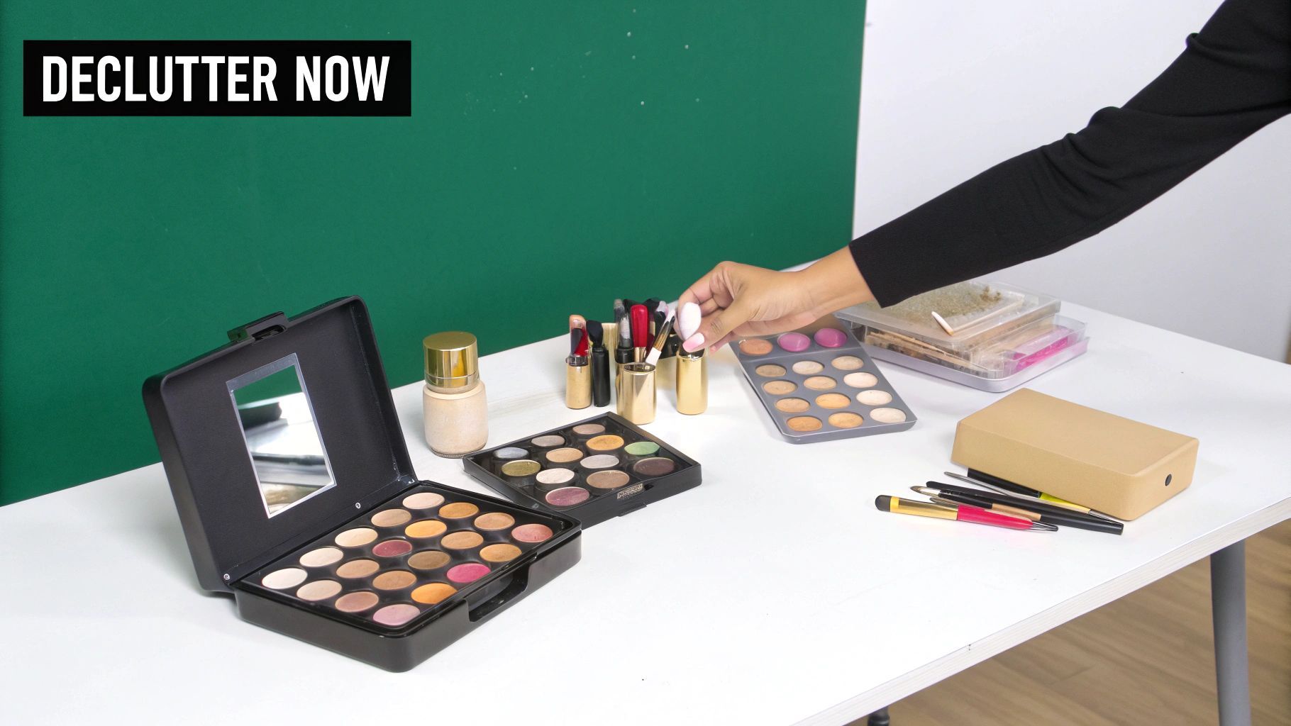 A person's hand selects a makeup brush from an array of cosmetics on a white table.