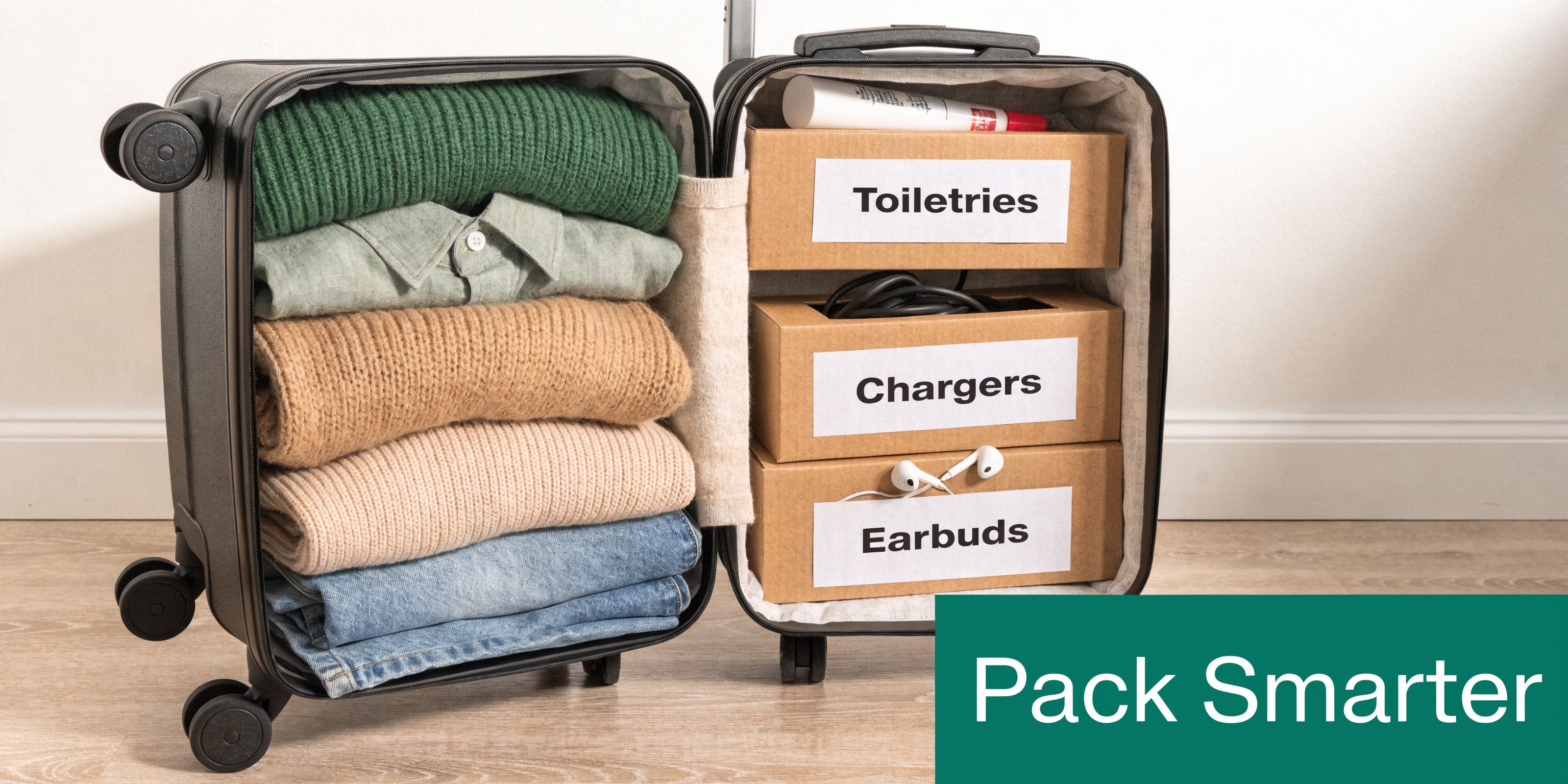 An open suitcase neatly organized with folded clothes on one side and labeled storage boxes for items.