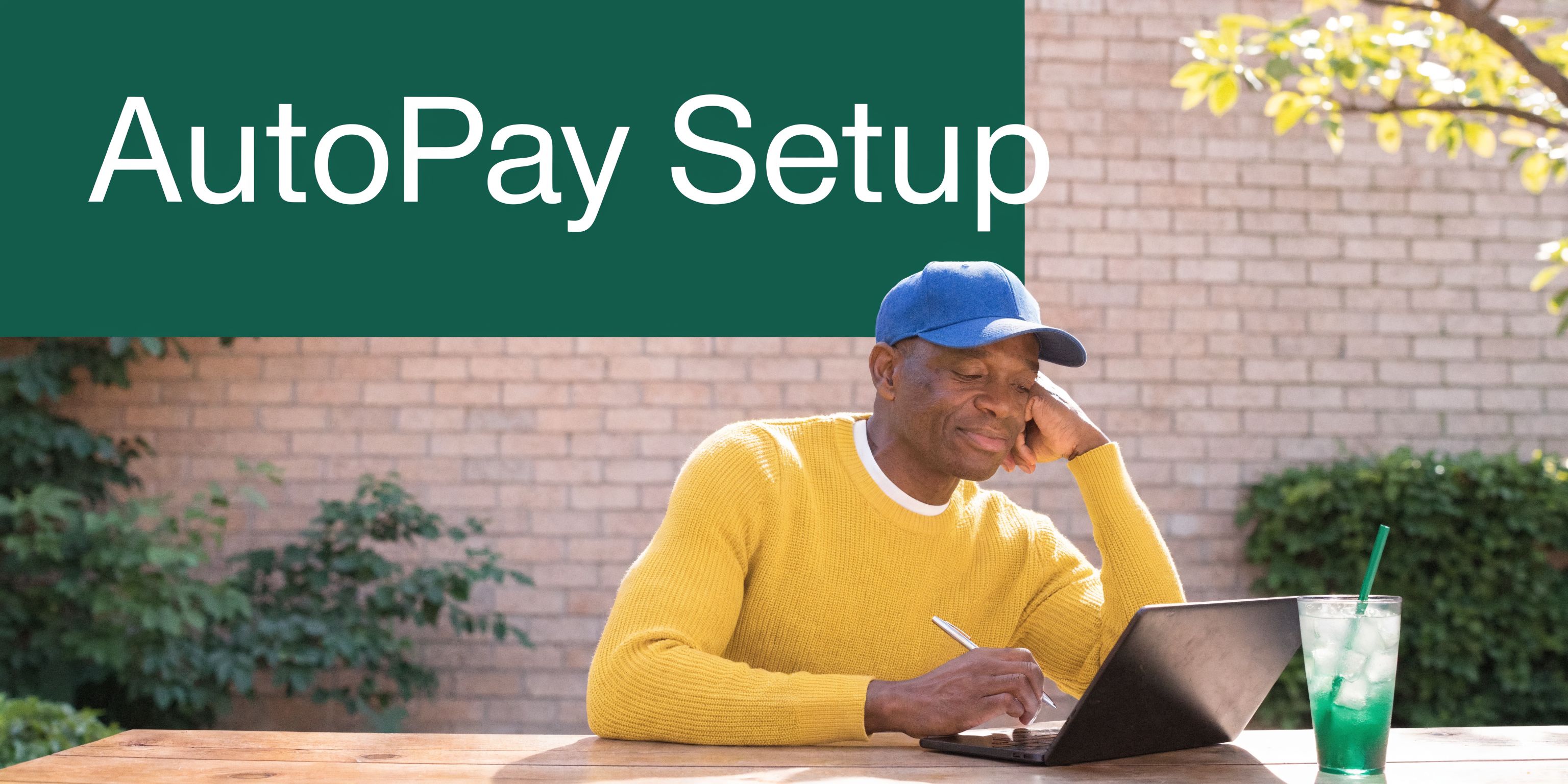 A man in a yellow sweater using a laptop at an outdoor table for AutoPay setup.