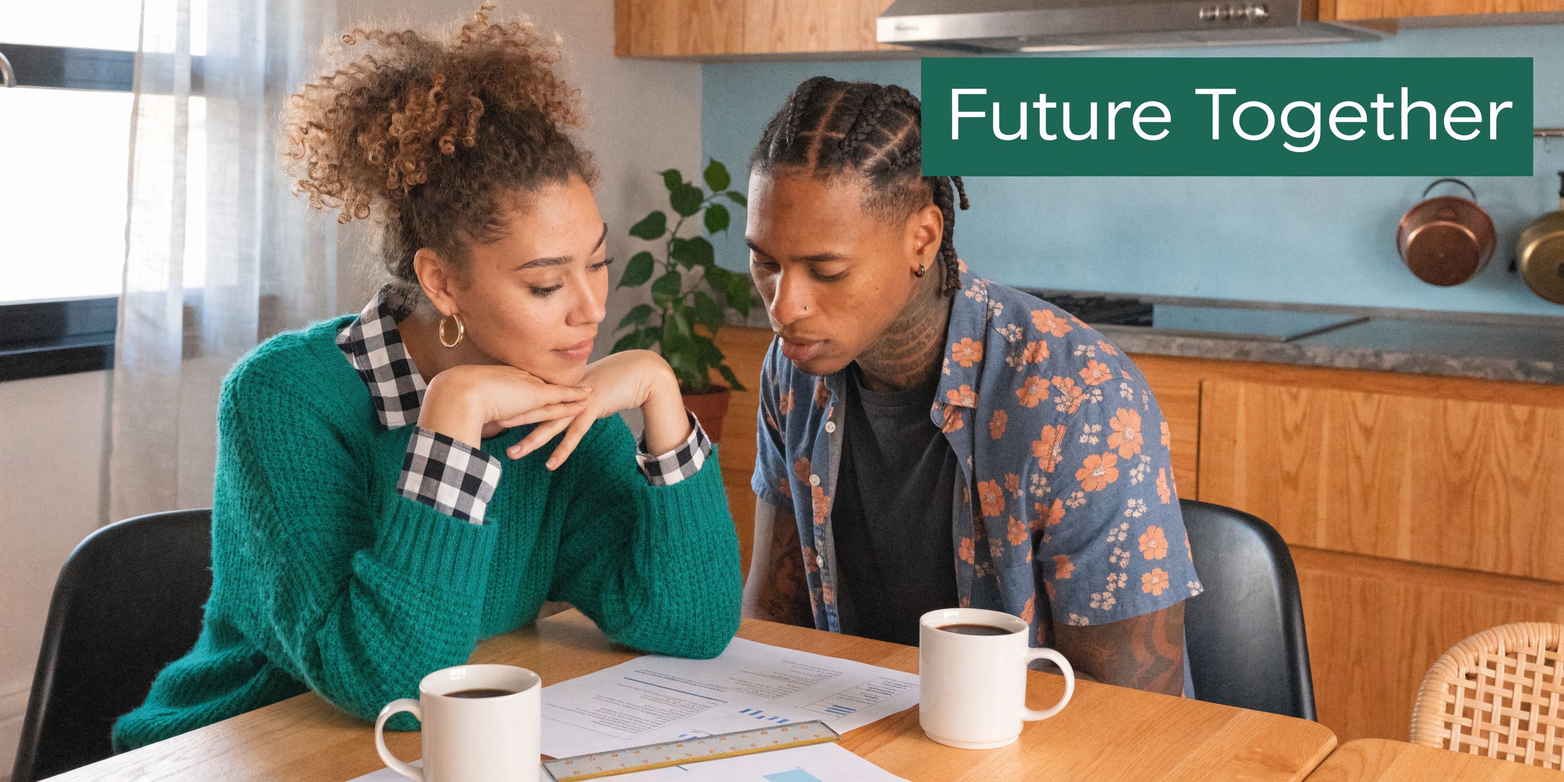 A young couple sitting at a wooden kitchen table, looking thoughtfully at financial documents together.