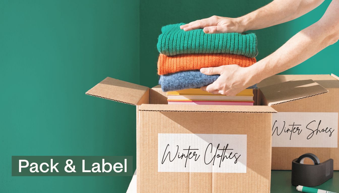 A person packing folded winter sweaters into a cardboard box labeled Winter Clothes for storage purposes.