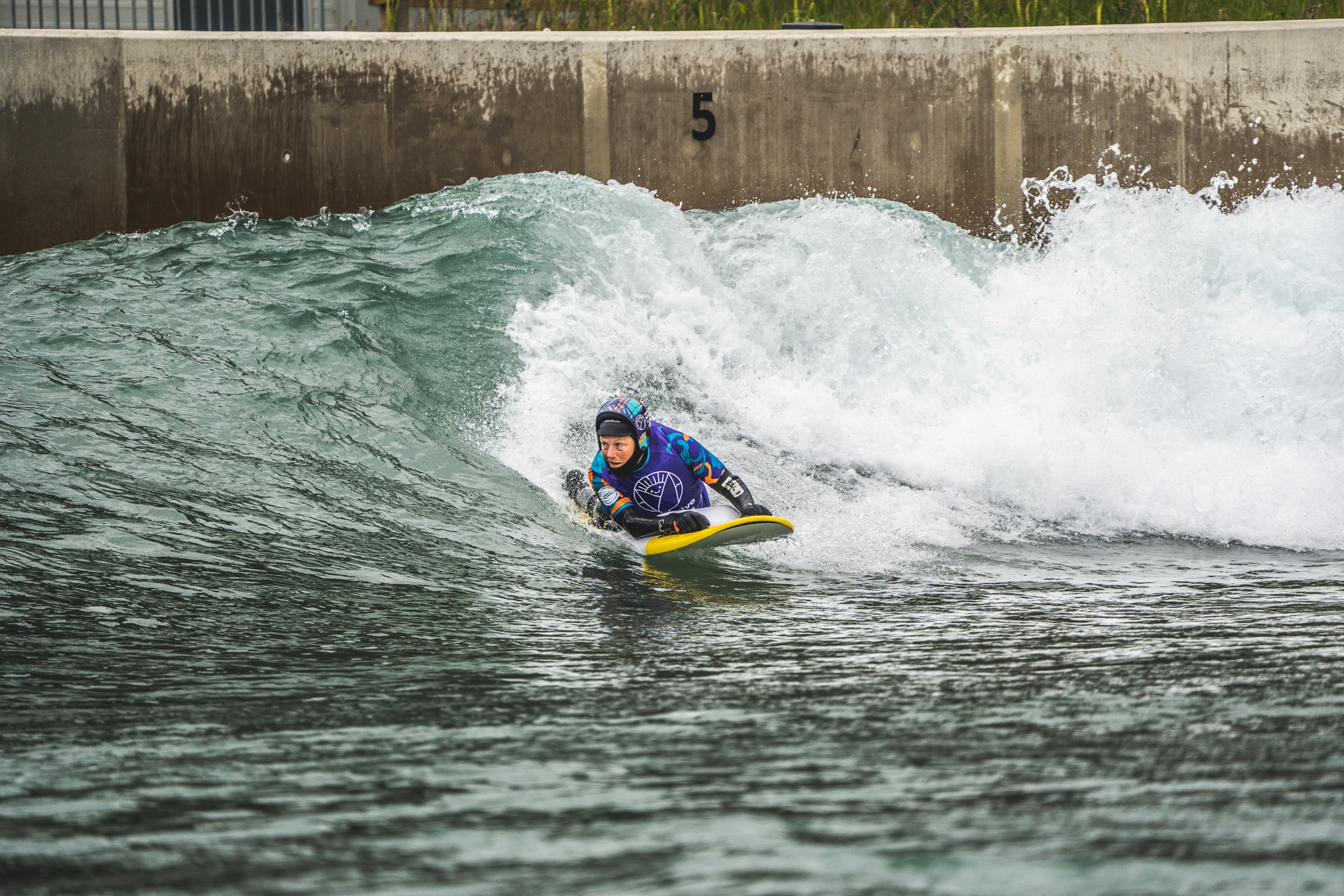 Surfer rides in a prone position across a wave