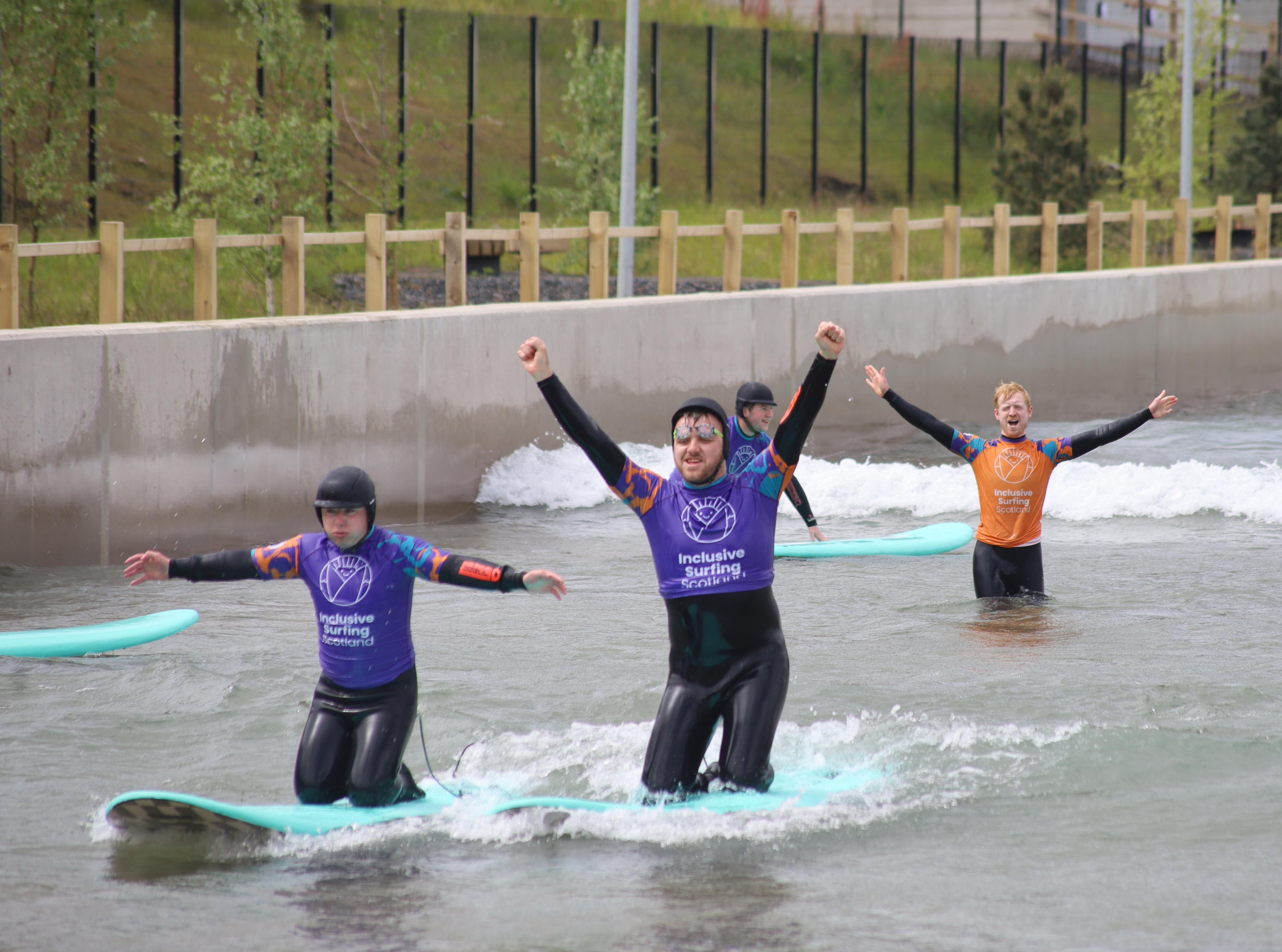 Surfer riding a wave in a prone position, with a coach in the background