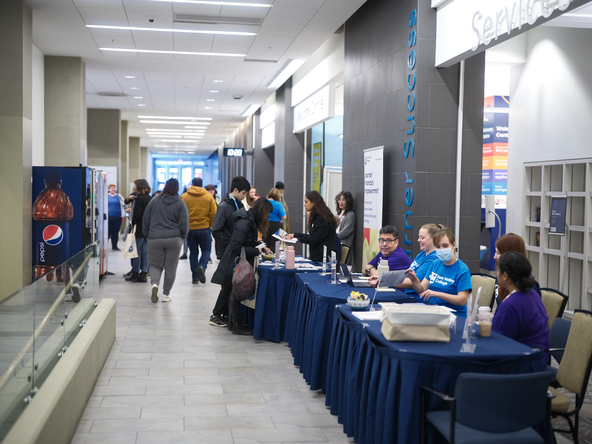 A hallway at Bow Valley College South Campus lined with tables for the Open House event with prospective students talking to staff.