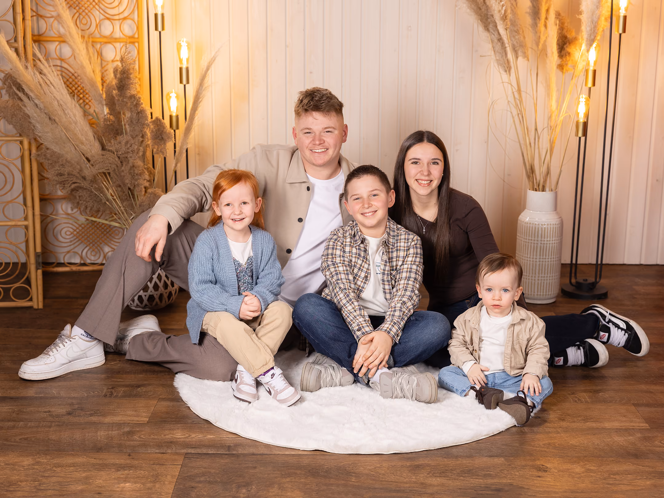 Glückliche Familie mit zwei Mädchen und zwei Jungen vor warmem, dekorativem Hintergrund sitzend.