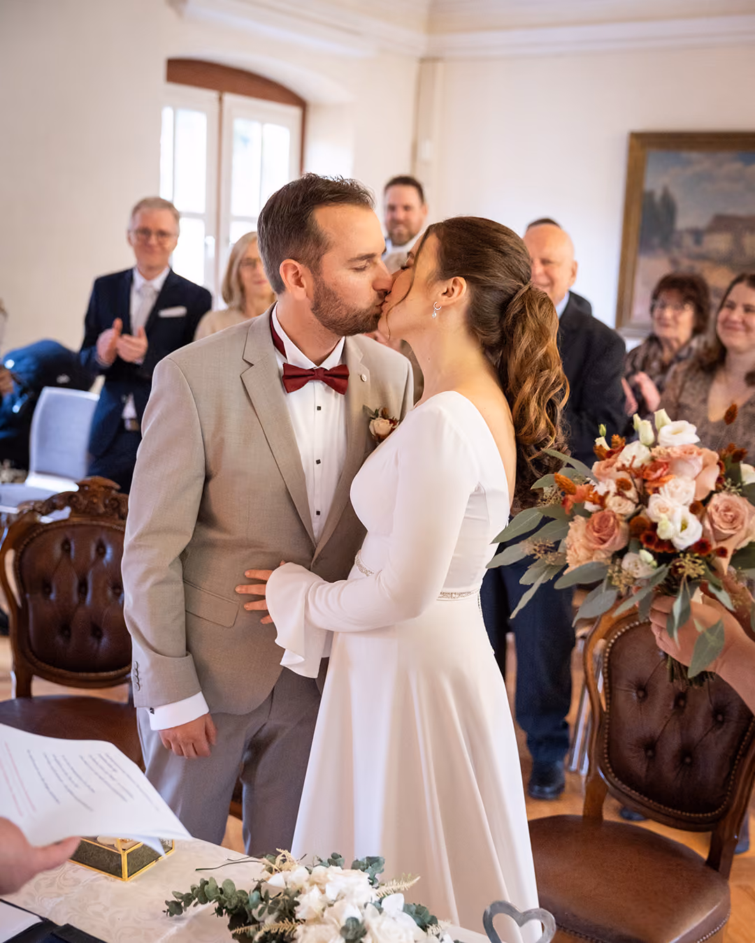 Braut und Bräutigam küssen sich bei der Trauung, während Gäste im Hintergrund applaudieren.
