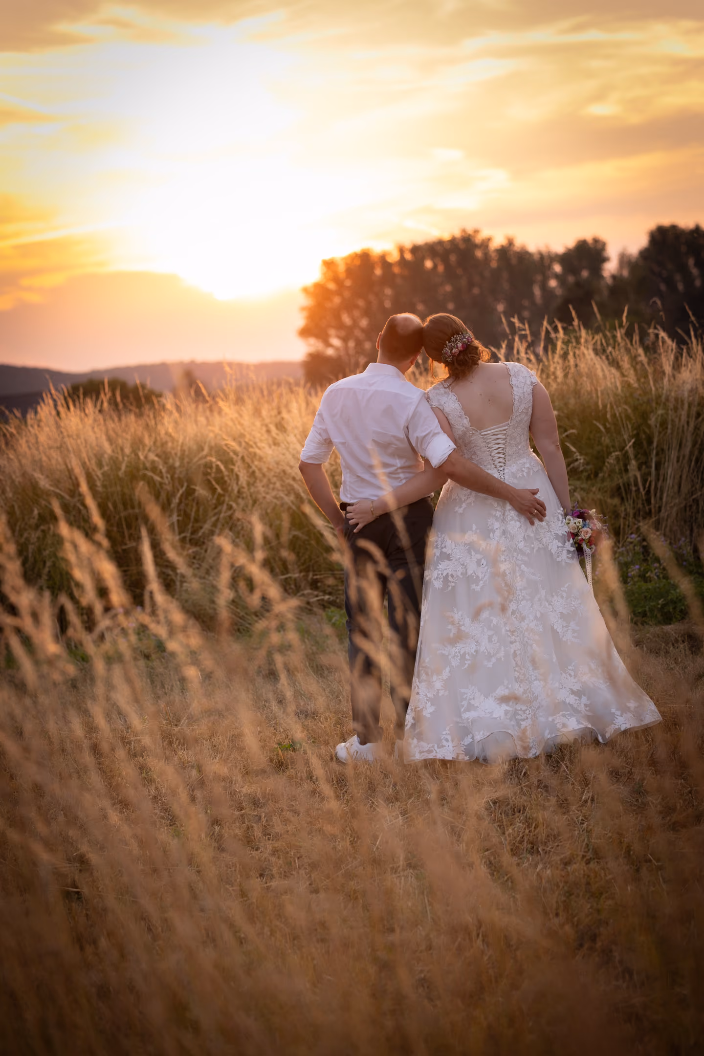 Braut und Bräutigam umarmen sich in einem Feld bei Sonnenuntergang.