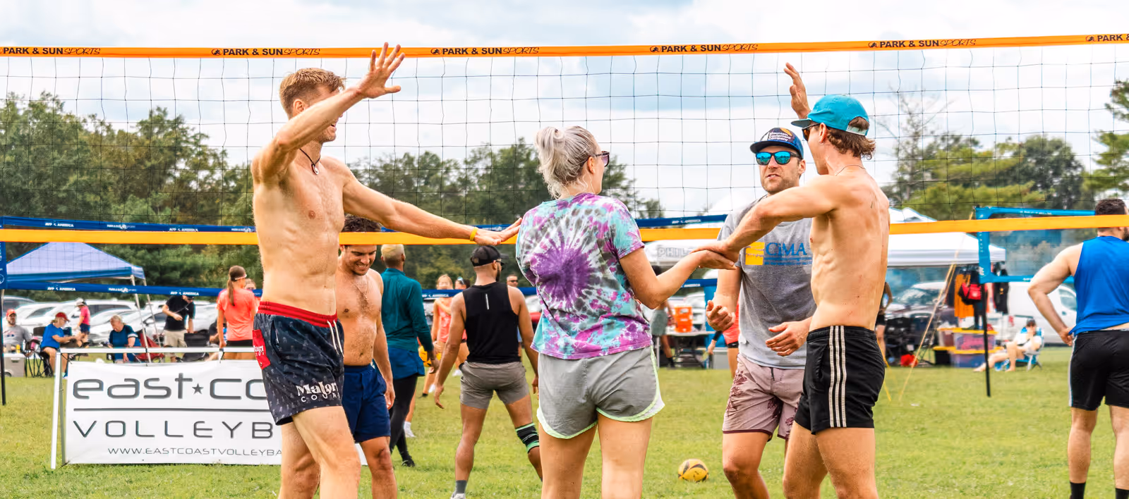 Group of people playing outdoor volleyball, celebrating near the net on a grassy field.