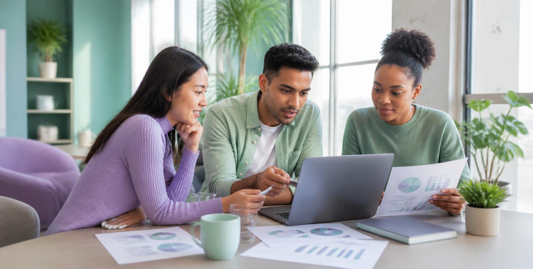 Three people discussing documents and a laptop around an office table