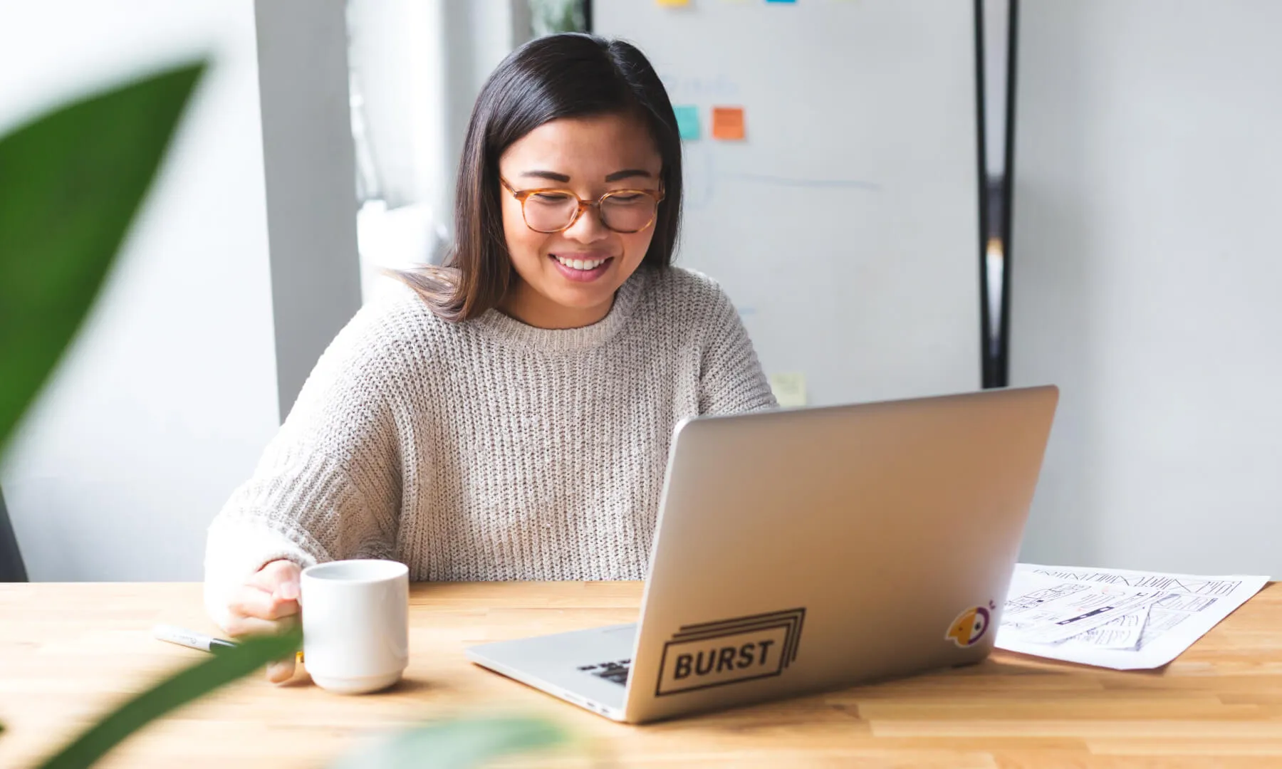 Stockphoto einer Frau, die mit einer Kaffeetasse in der Hand an einem Laptop sitzt