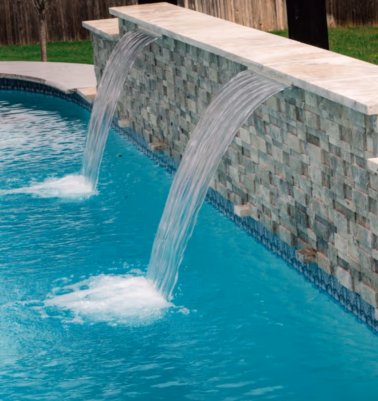 New pool build in New Braunfels, Texas featuring a turquoise swimming pool with elegant cascading water features on a stone wall.