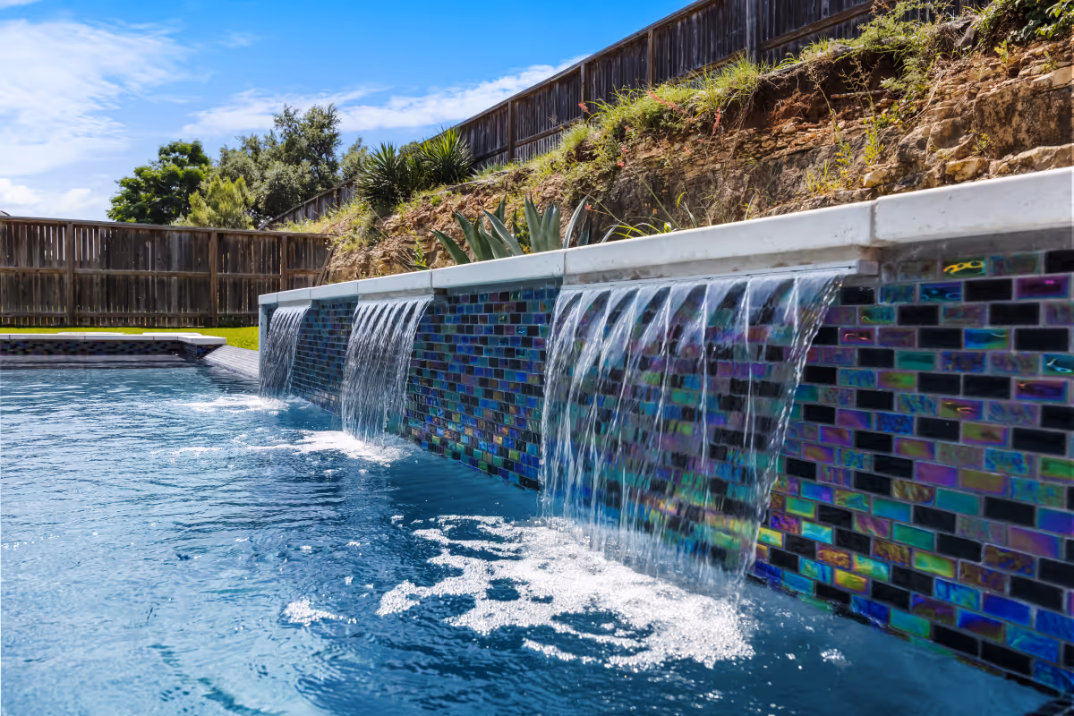 New modern pool in Boerne, TX featuring vibrant tile and cascading waterfalls on a sunny day