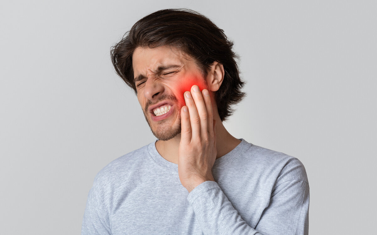 Patient grimacing with tooth pain holding jaw, illustrating symptoms of cavity and toothache at dental clinic