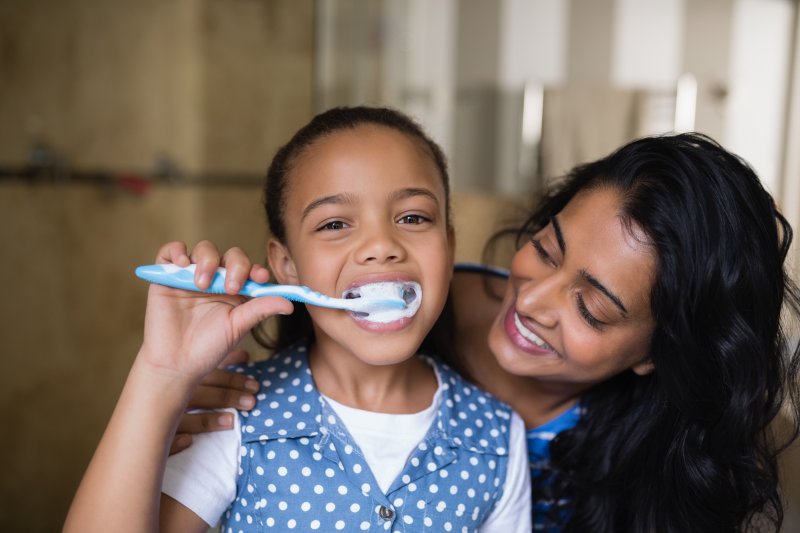 Happy child brushing teeth with parent showing proper children oral hygiene habits.
