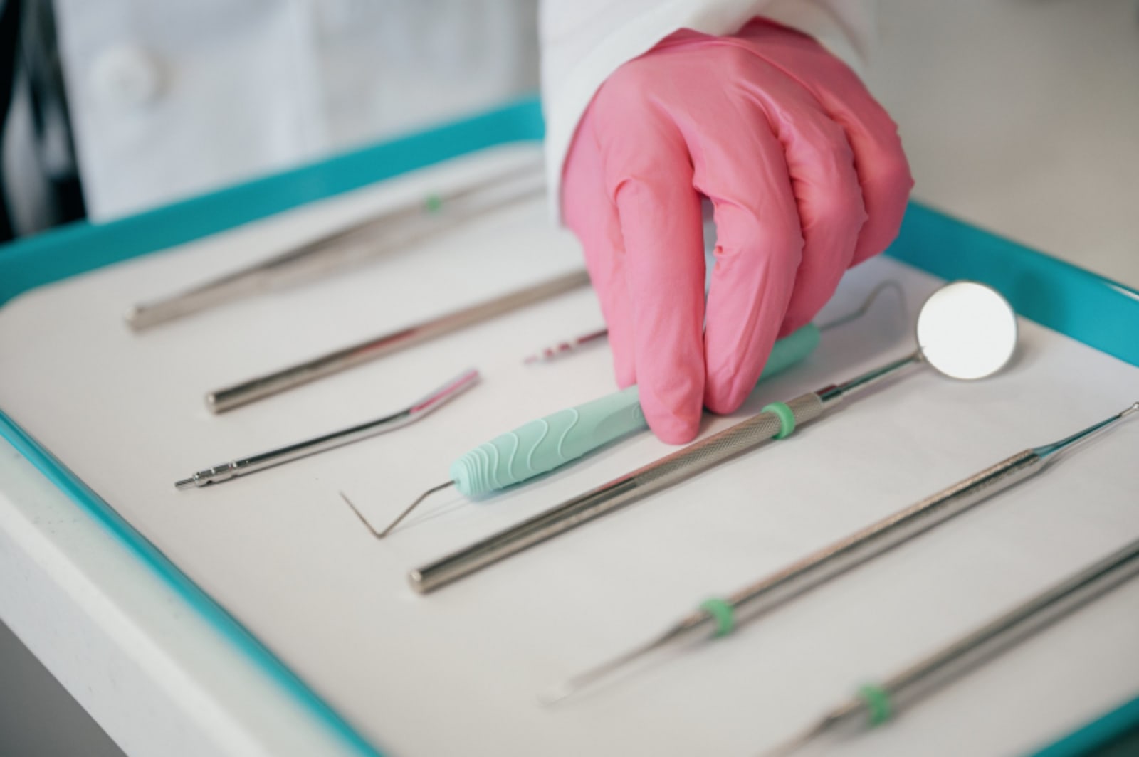 Dental instruments laid out on tray with hands wearing pink gloves