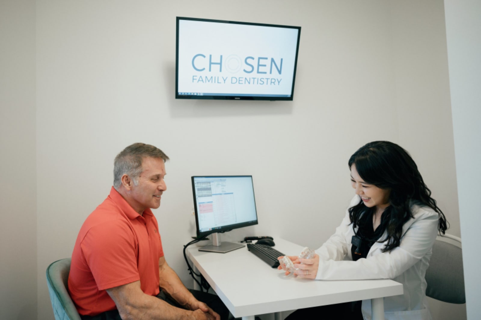 Dentist in coral shirt consulting with patient at front desk