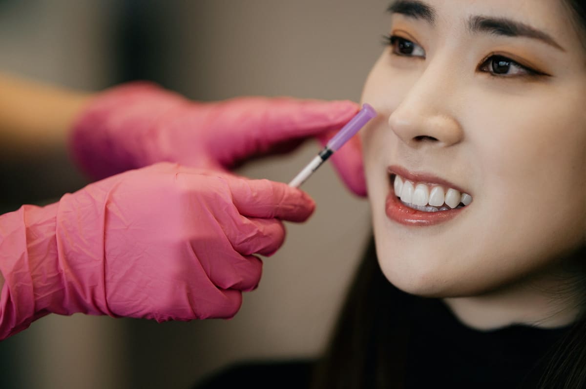 Dentist in pink gloves demonstrating clear aligner placement on patient's smile