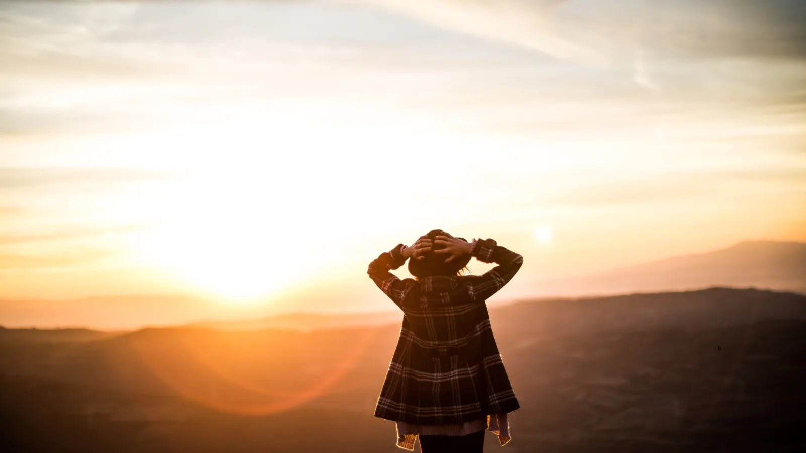 A child standing on a hillside at sunset.