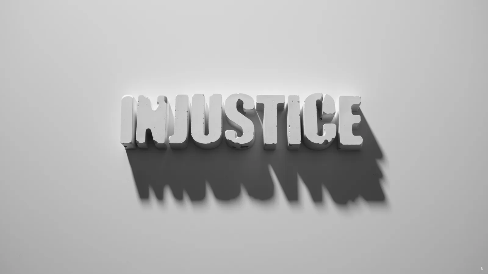 The word “injustice” cast in white letters with a long shadow on a pale wall.