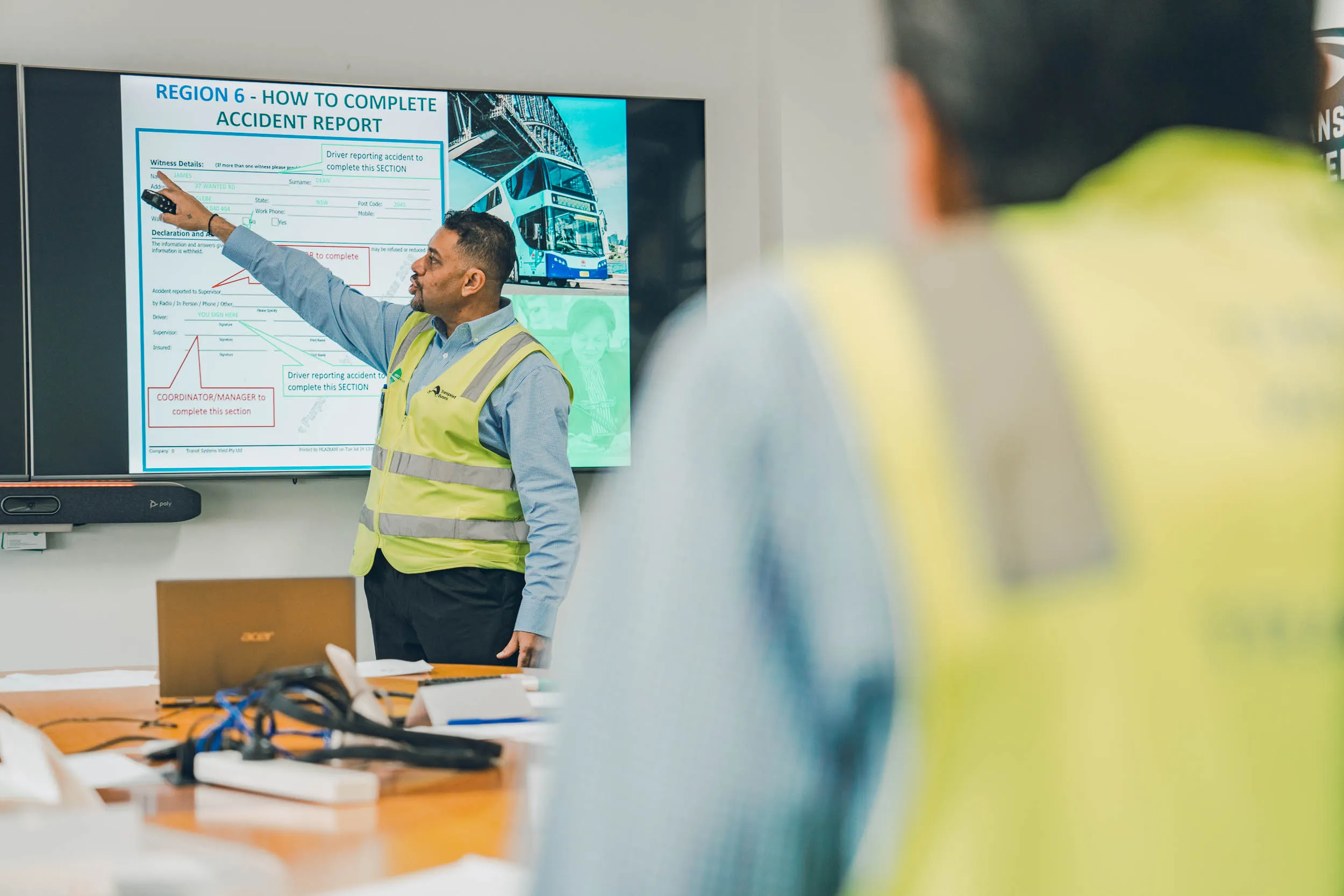 Man in safety vest pointing at screen showing instructions on completing an accident report.
