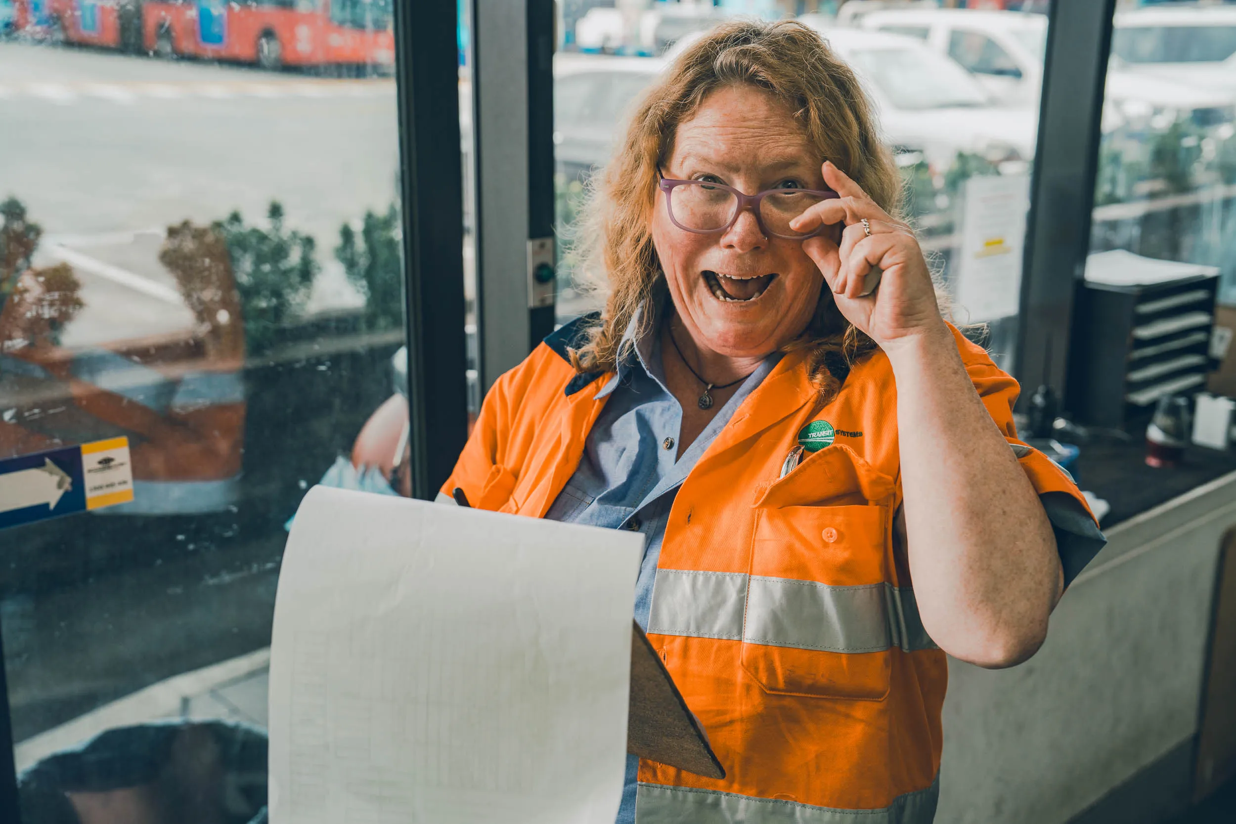 Woman in orange safety vest holding clipboard and adjusting glasses expressing surprise or excitement.