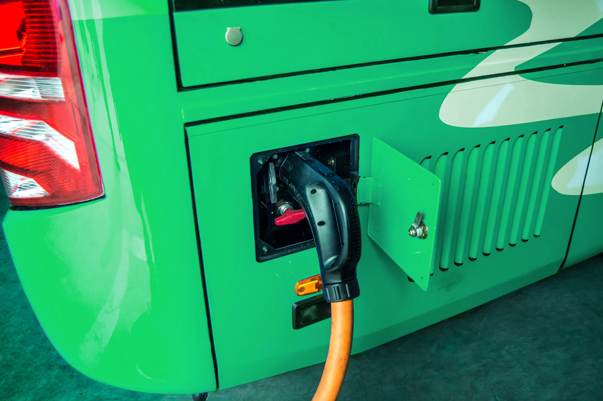 Close-up of a green electric bus being charged with an orange charging cable plugged in.
