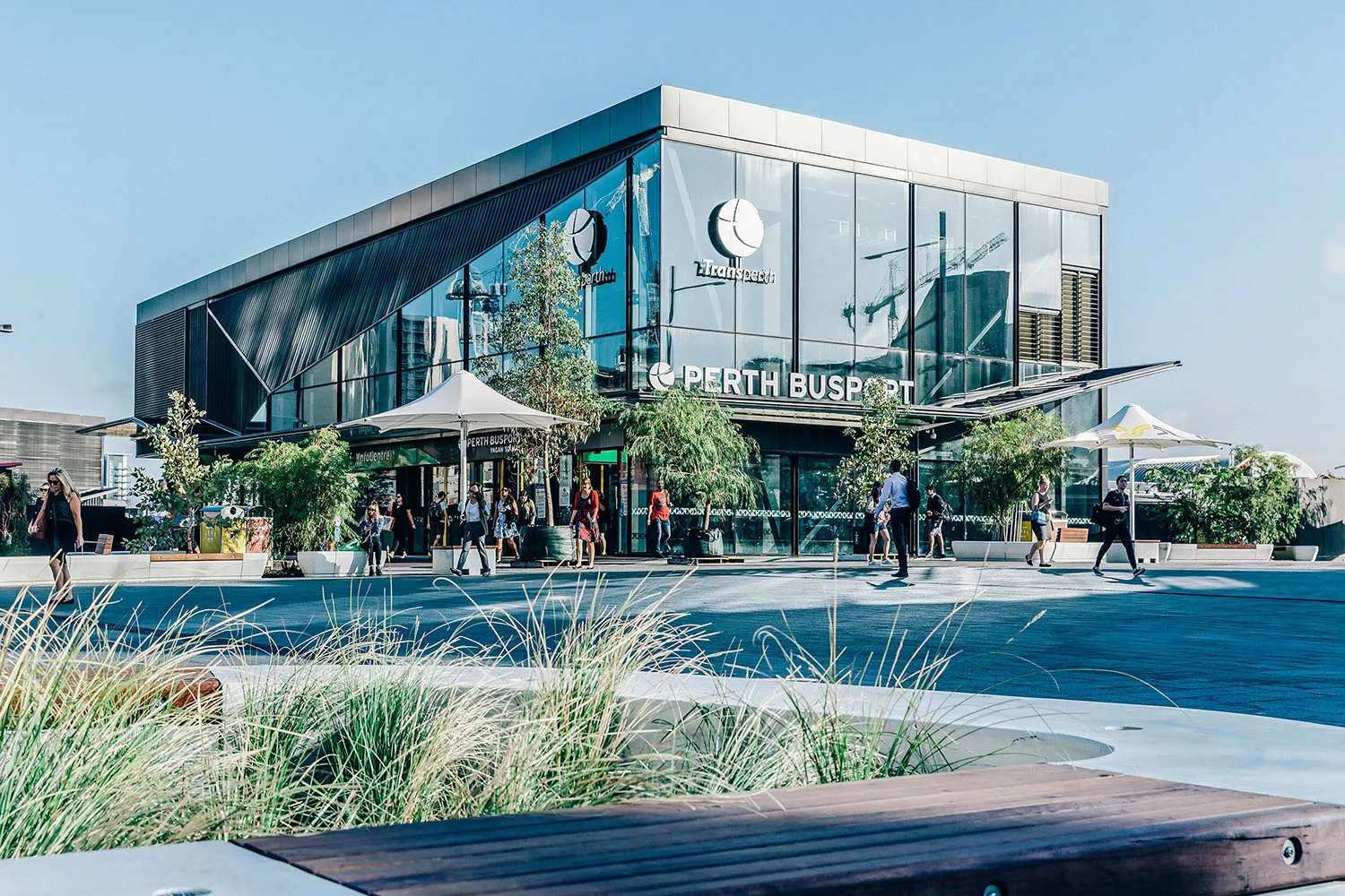 Modern glass building with Perth Busport signage and people walking outside on a sunny day.