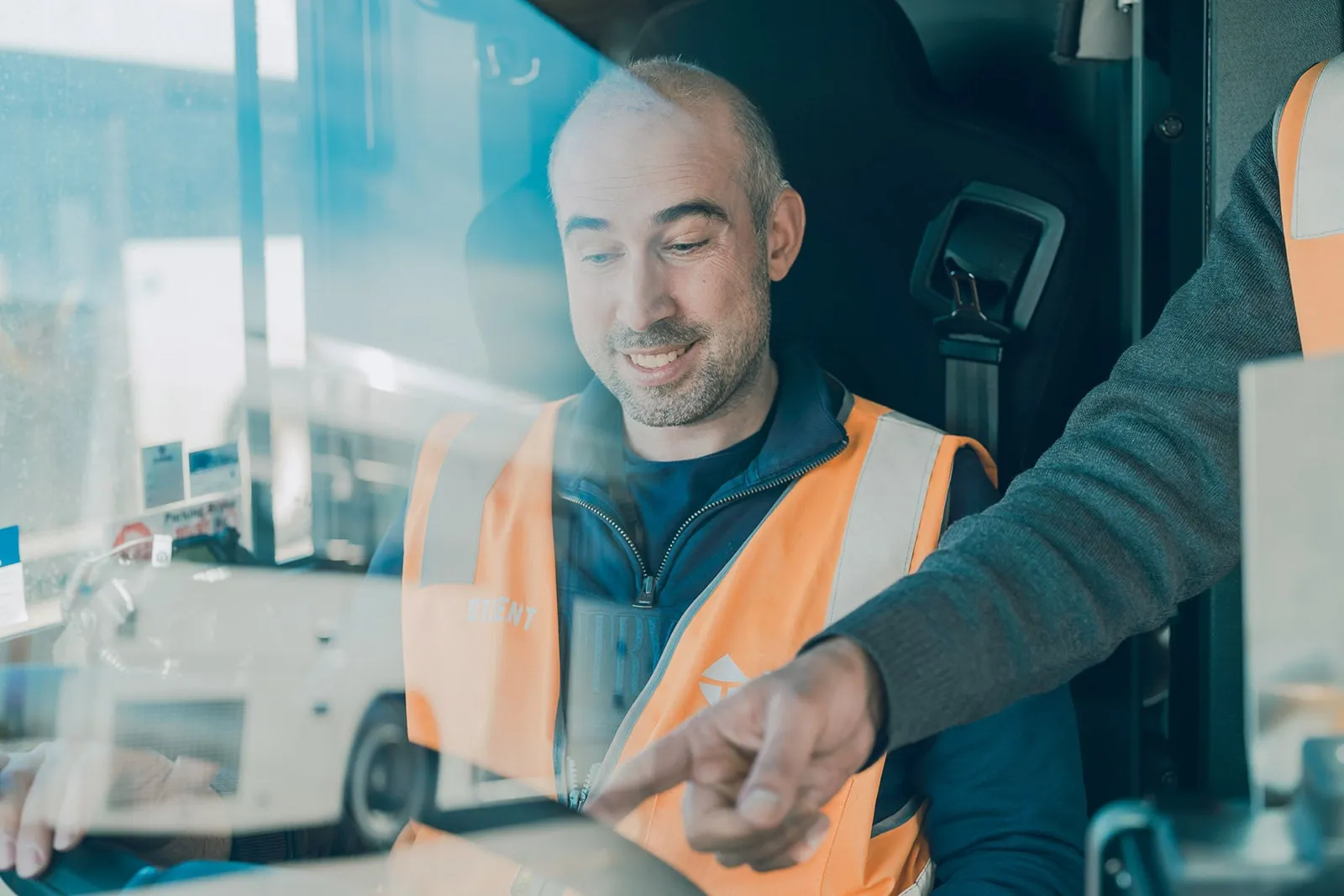 Smiling man in orange safety vest looking at a tablet while another person points at it.