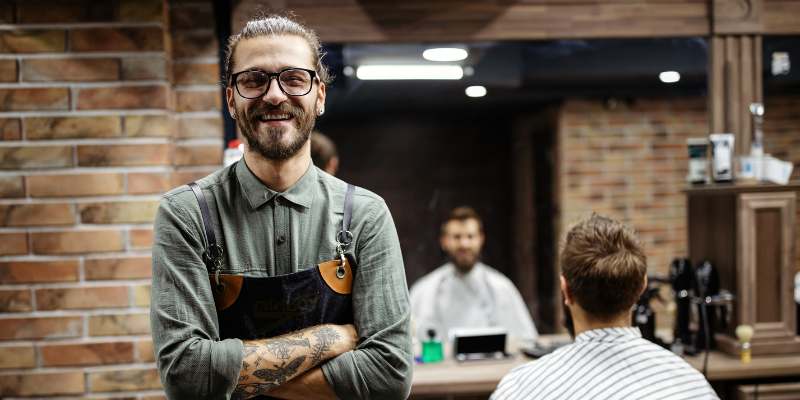 Barbershop worker smiling with customer sitting on a chair in the background