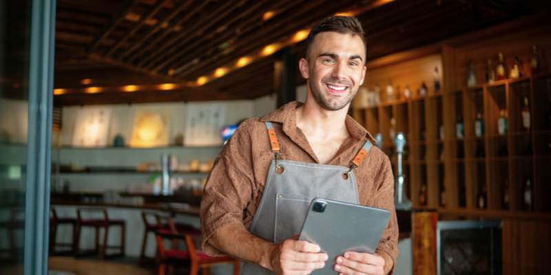 Restaurant owner smiling holding ipad about getting Bizcap's Line of Credit loan