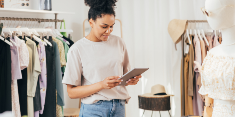 Retail clothing brand business owner smiling looking at tablet in shop